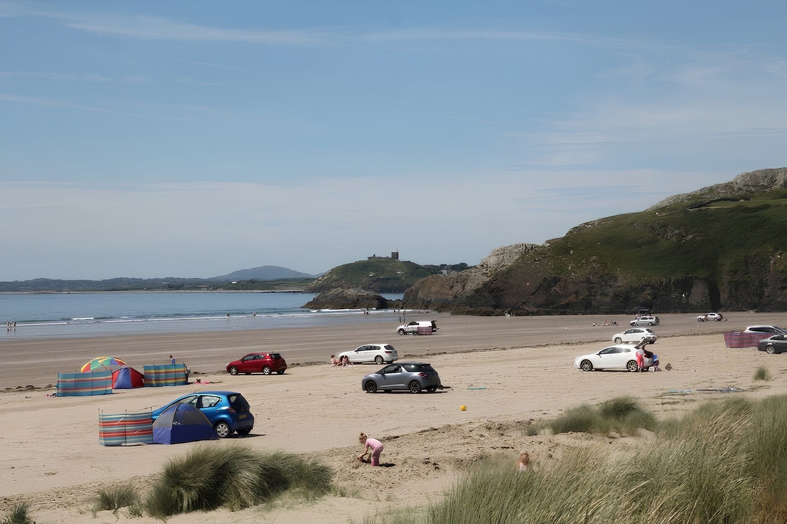 Une plage avec des tentes, des voitures et une colline herbeuse.