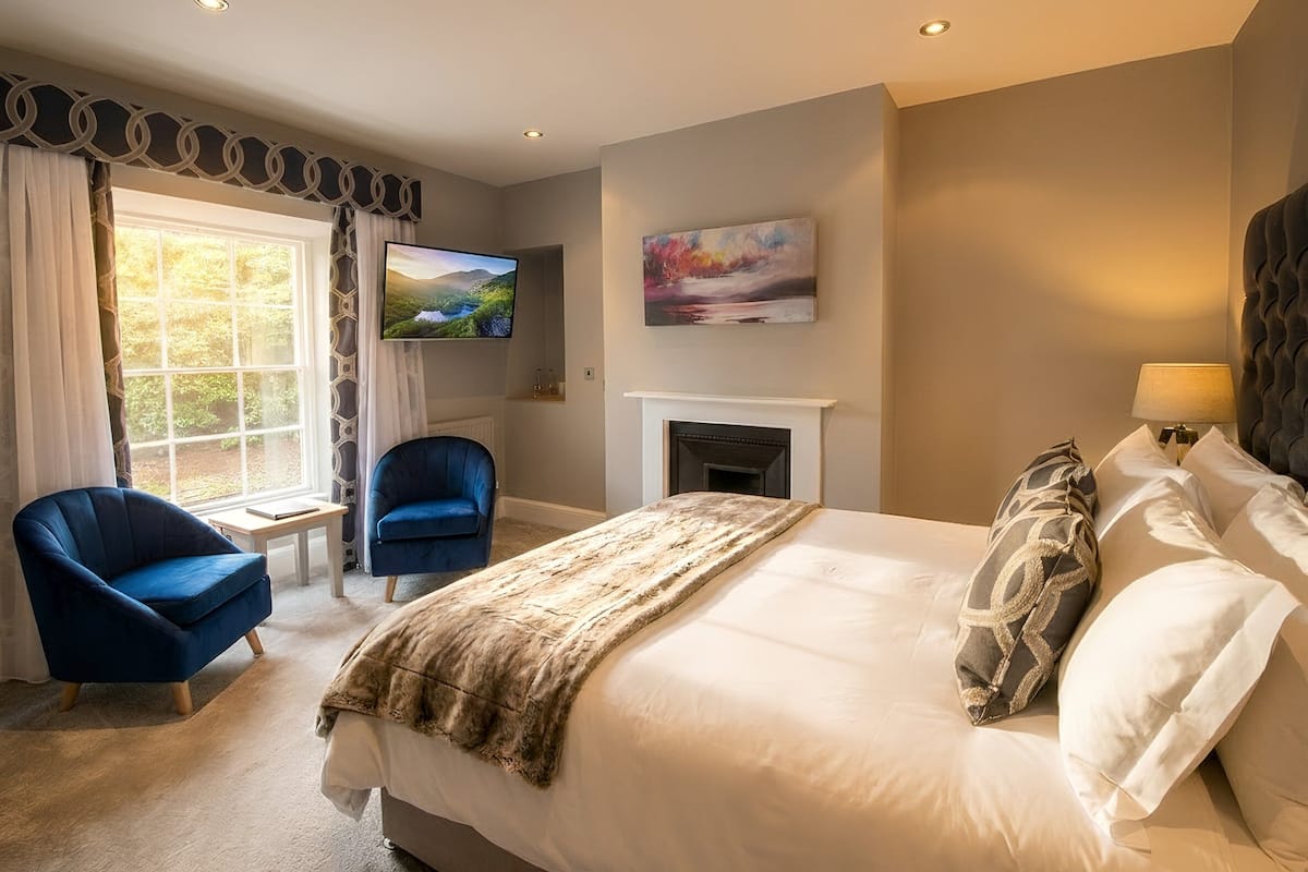 A bedroom with a bed, a TV, a fireplace, and a window.