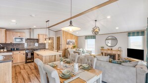 A modern kitchen with wooden cabinets, a dining area with a wooden table and chairs, and a living area with a sofa and a fireplace. - Aberdunant Hall (Porthmadog)
