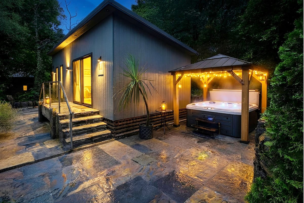 A modern house with a hot tub, stone steps, and a wooden pergola with string lights.