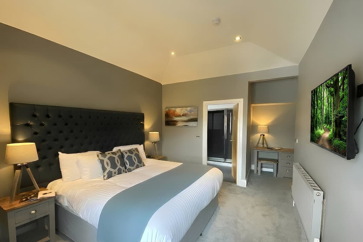 A bedroom with a large bed, bedside lamps, a headboard, a painting, a desk, and a radiator.