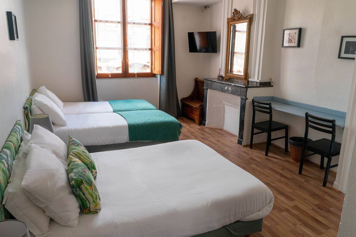 A hotel room with two beds, a desk, a chair, a TV, and a mirror.