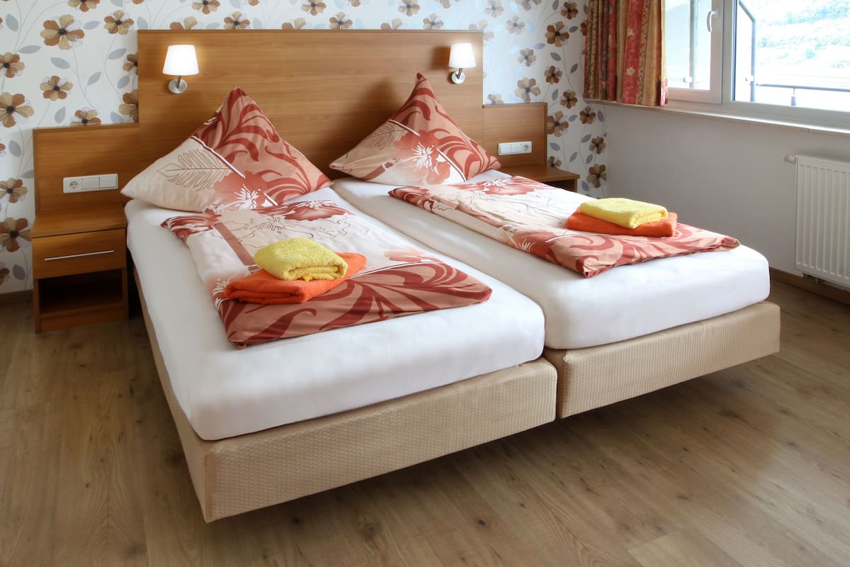 A double bed with floral-patterned bedding, a nightstand with a lamp, and a window with curtains.