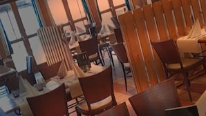 Un restaurante con mesas y sillas de madera, ventanas amplias y suelo de baldosas.