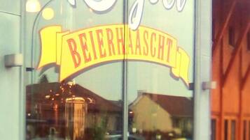 Ein Gebäude mit einem großen Fenster, das verschiedene Waren ausstellt. Auf dem Fenster steht der Schriftzug "15 Joër BEIERHAASCTT".