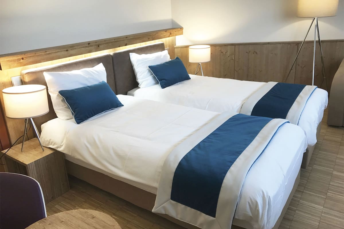 Una cama doble con ropa de cama blanca y azul, dos lámparas de noche y un cabecero de madera.