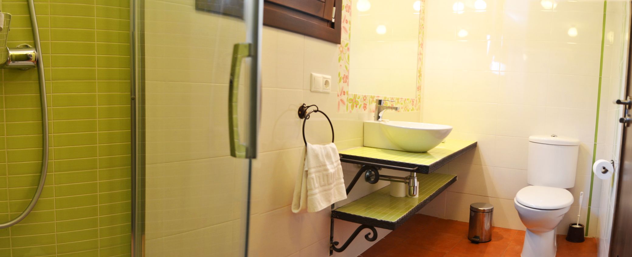 A bathroom with a green-tiled shower, a sink with a mirror above it, and a toilet.