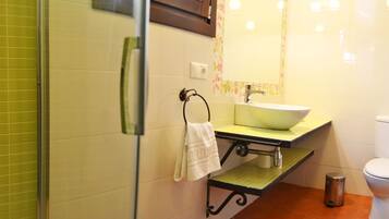 A bathroom with a green-tiled shower, a sink with a mirror above it, and a toilet.
