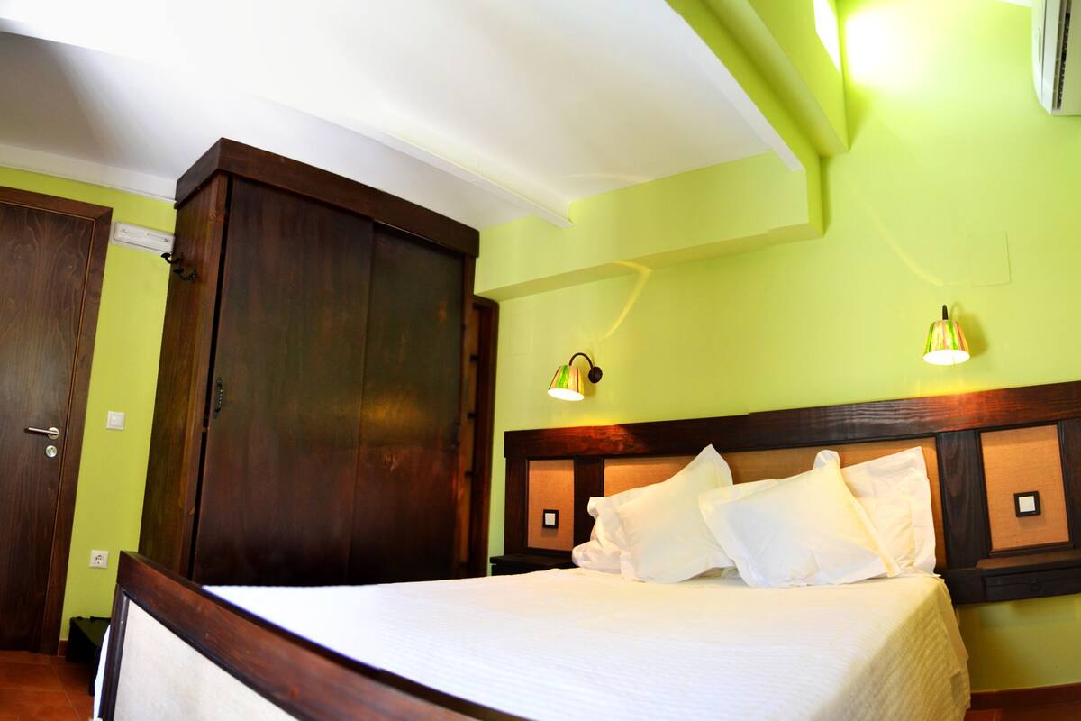 Una habitación de hotel con una cama, un armario de madera y dos lámparas fijadas a la pared.