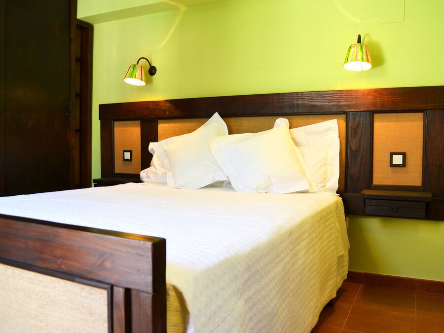 Una cama bien tendida con sábanas blancas en una habitación con paredes verdes y cabecera de madera.