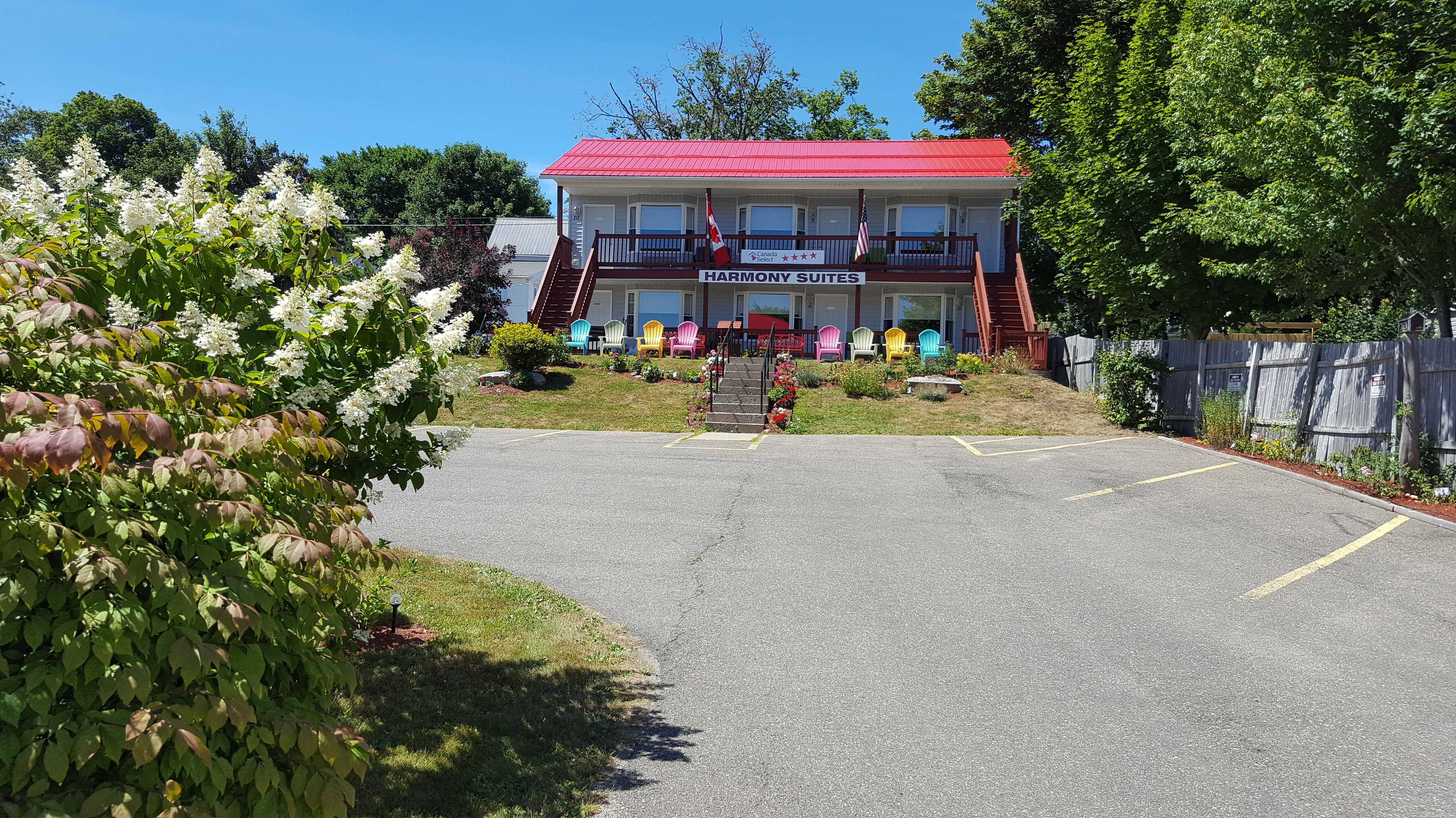 A Harmony Suites building with a red roof, a porch with colorful Adirondack chairs, and a parking lot.