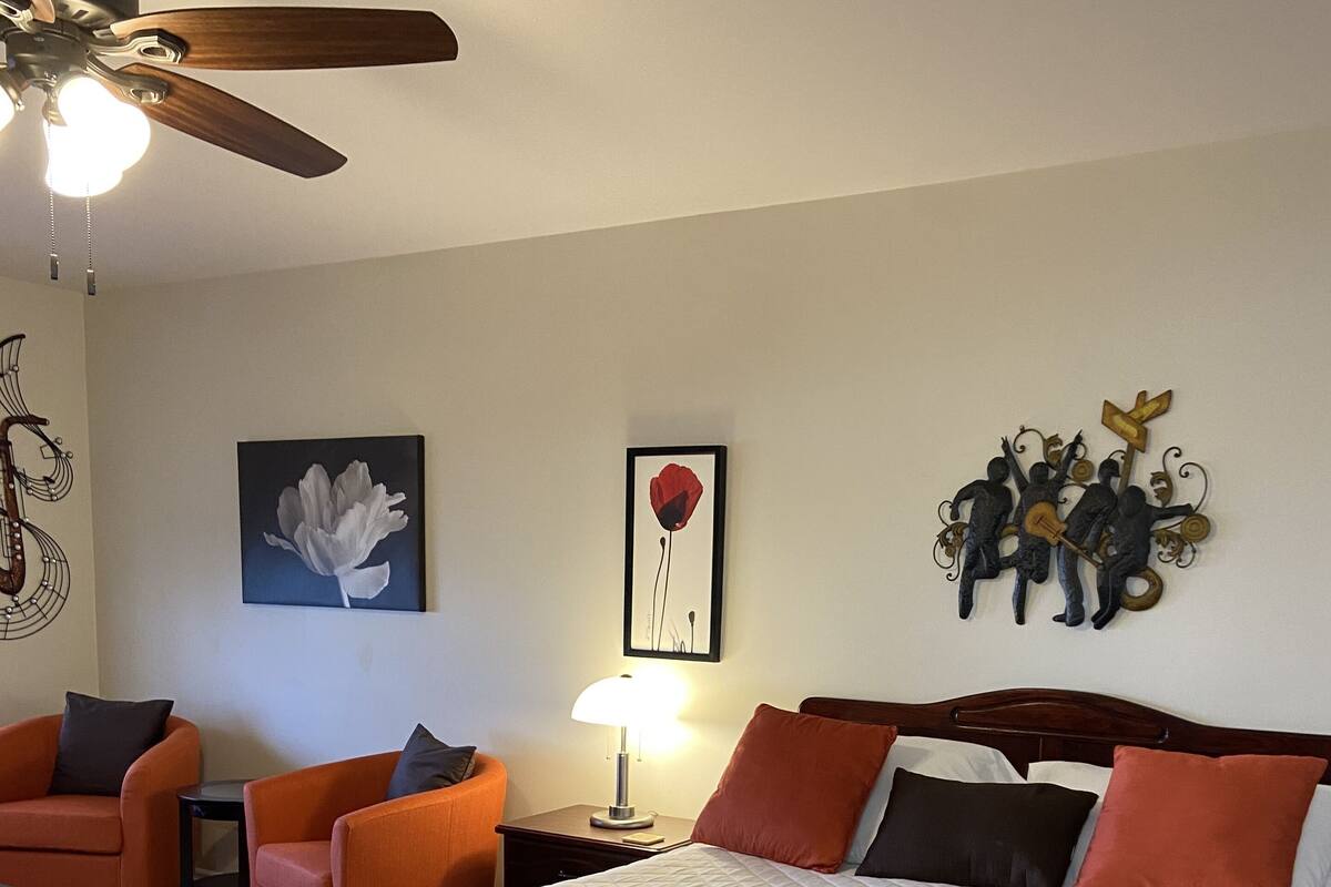 Une chambre d’hôtel comprenant un lit, deux chaises, une table de chevet, une lampe et des œuvres d’art murales.