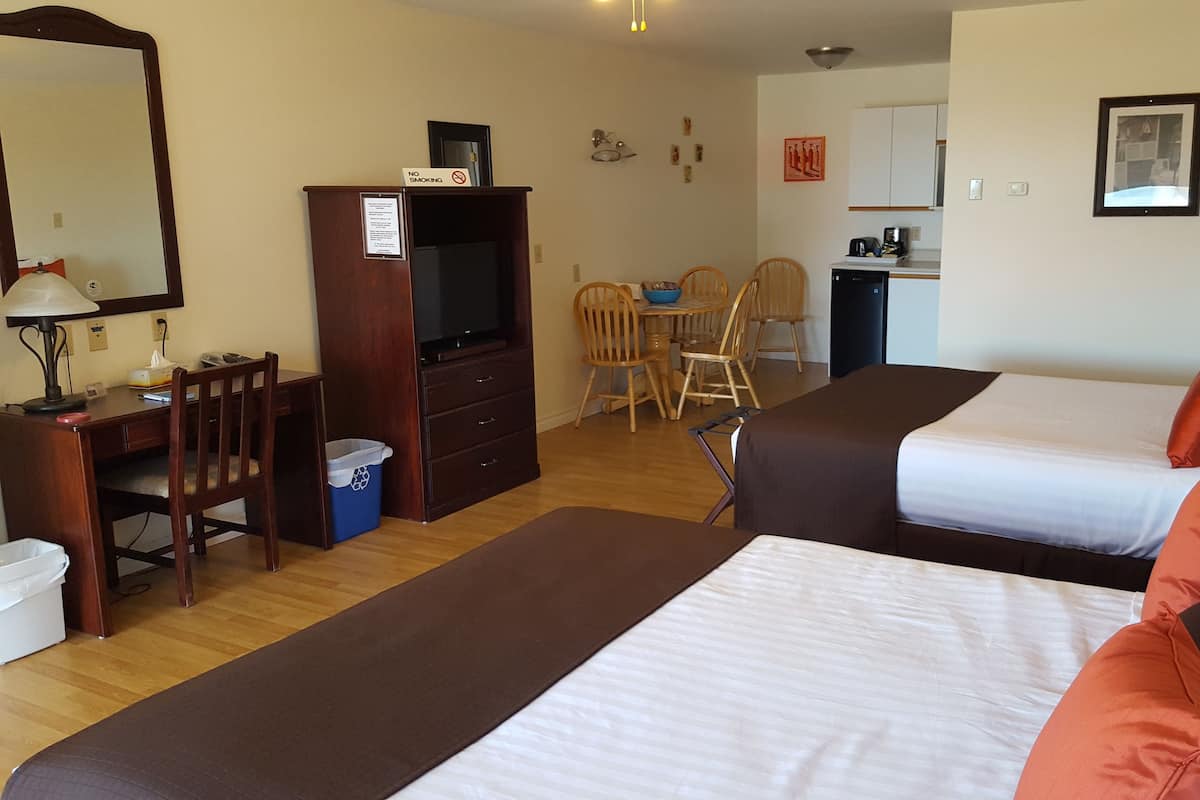 Une chambre d’hôtel avec deux lits, un bureau avec un ordinateur, une télévision, un coin repas avec des chaises et un coin cuisine.