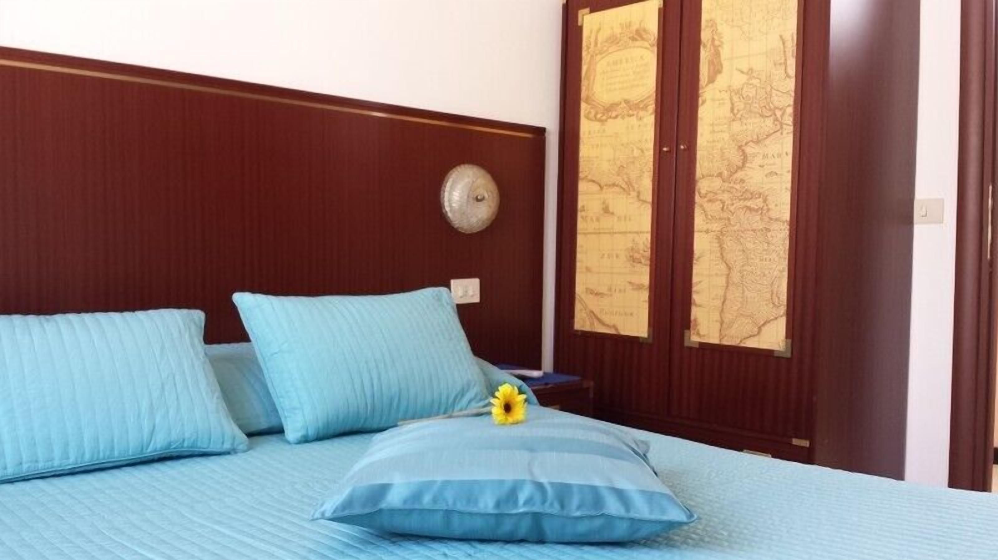 Uma cama com roupa de cama e almofadas azuis, um relógio na parede e um mapa.