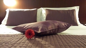 A bed with a brown quilt, two dark pillows, and a red flower.