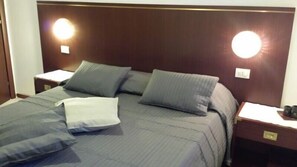 A neatly made bed with grey bedding and pillows, two bedside tables with lamps, and a dark wood headboard.