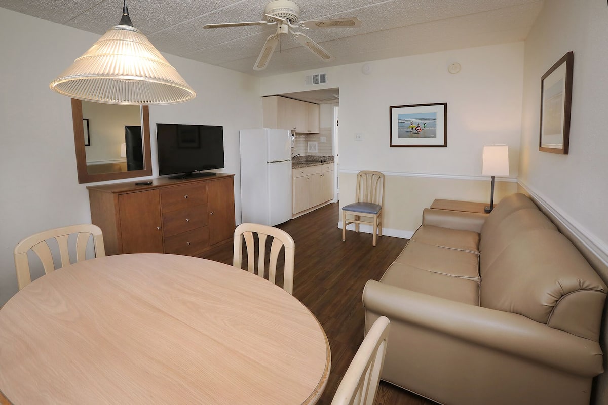 A compact living space with a dining area, a sofa, a kitchenette, and a ceiling fan.