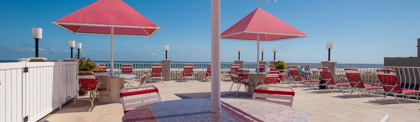 A rooftop terrace with red umbrellas, lounge chairs, and a view of the ocean.