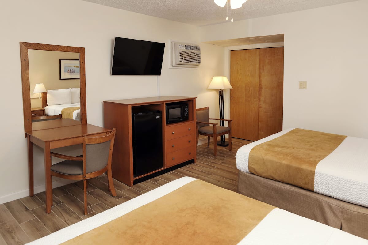 A hotel room with a wooden desk, a television mounted on the wall, a bed with a brown blanket, and a wooden wardrobe.