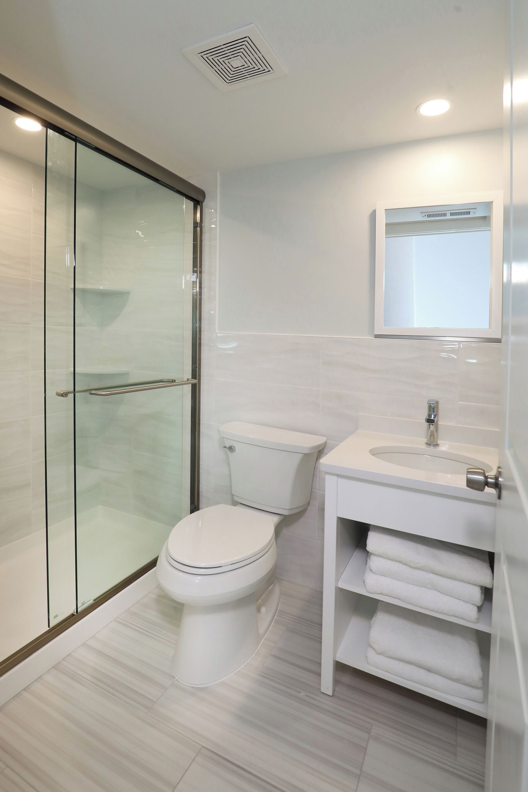Une salle de bain moderne avec une douche à parois de verre, des toilettes blanches et un meuble-lavabo doté d’un miroir et d’un porte-serviettes.