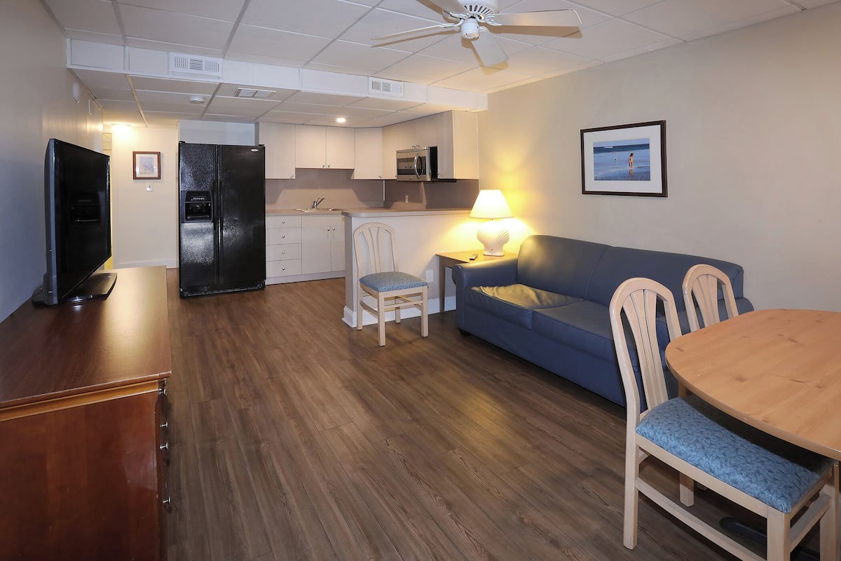 A compact living space with a kitchenette, a dining area with a wooden table and chairs, a blue sofa, and a ceiling fan.