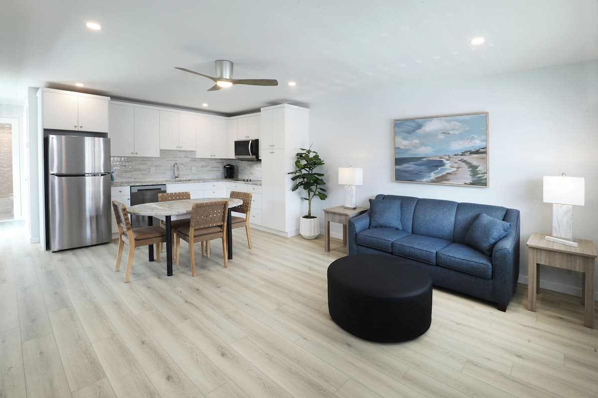 A modern kitchen with white cabinets, a stainless steel refrigerator, and a dining area with a wooden table and chairs.