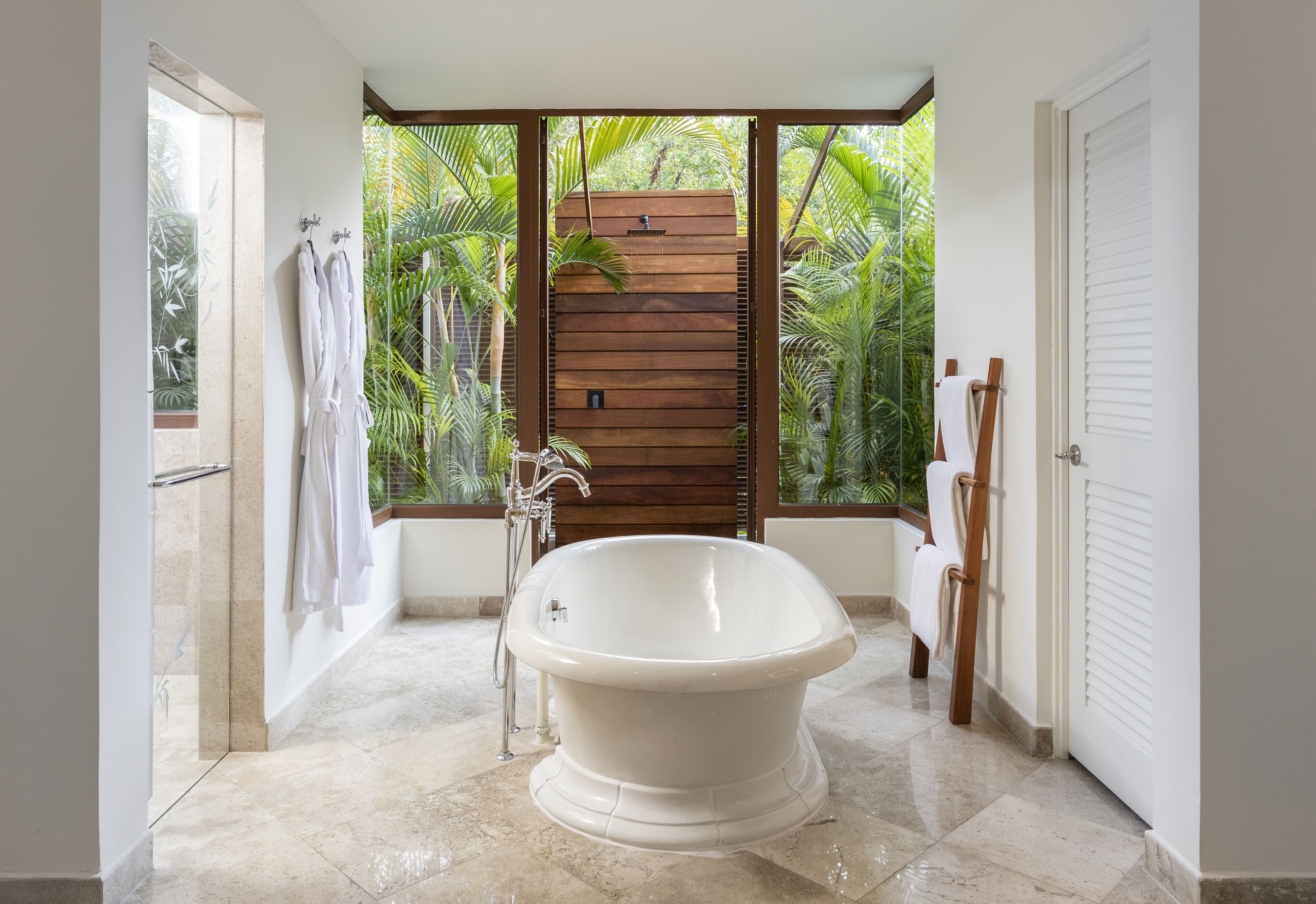 Un baño moderno con una bañera independiente, un panel de pared de madera y vistas a exuberante follaje.