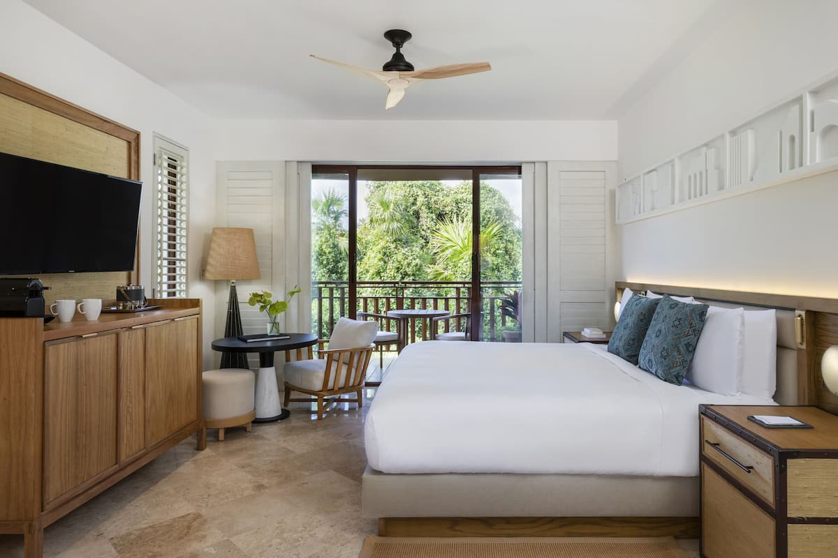 A hotel room with a bed, a desk, a television, a balcony with a view of greenery.