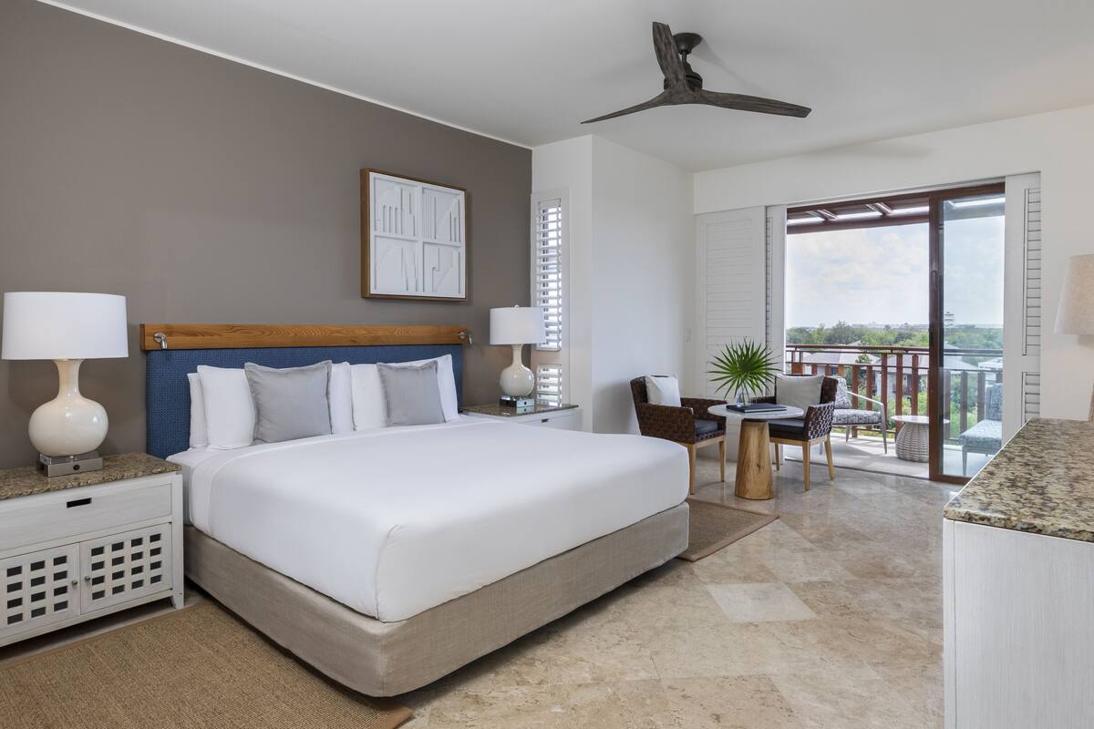 A hotel room with a large bed, a balcony with a view, and a ceiling fan.
