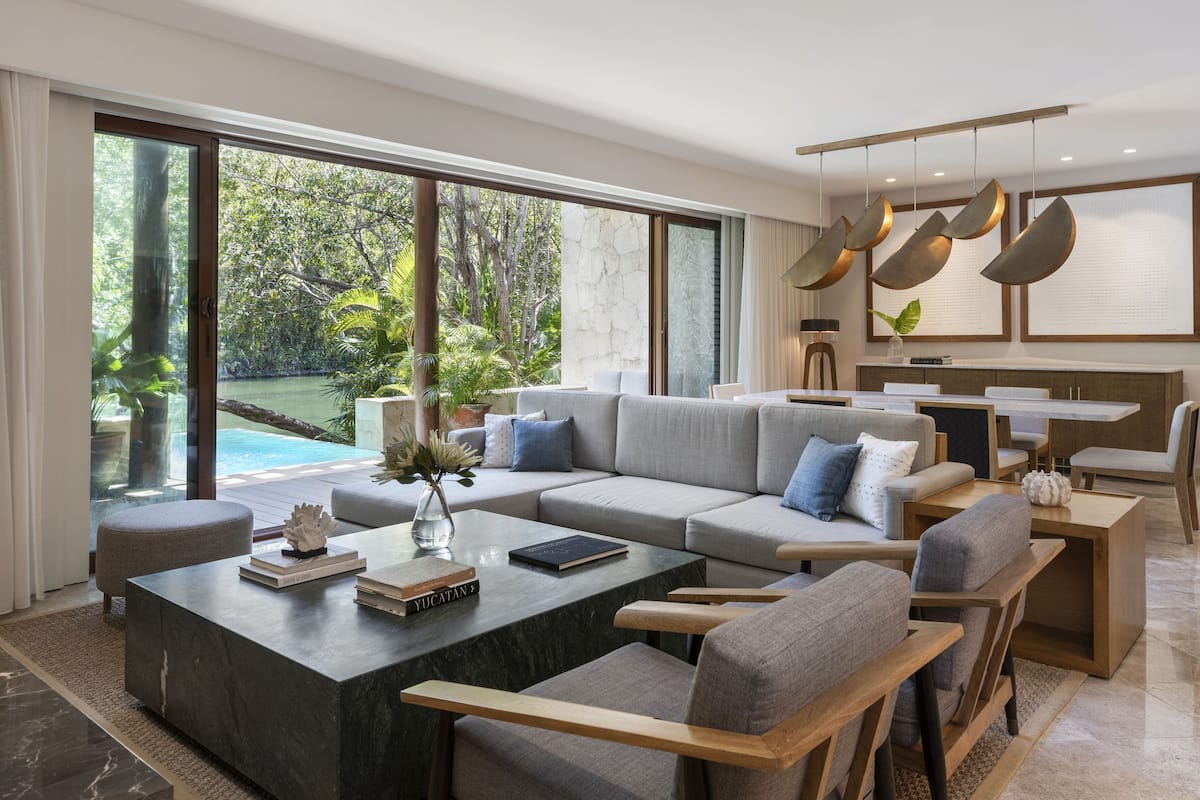 A modern living room with a large sectional sofa, a marble coffee table, and a view of a swimming pool.