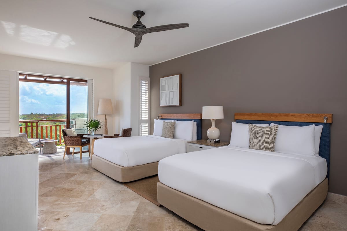 A hotel room with two beds, a balcony, a ceiling fan, and a view of the outdoors.