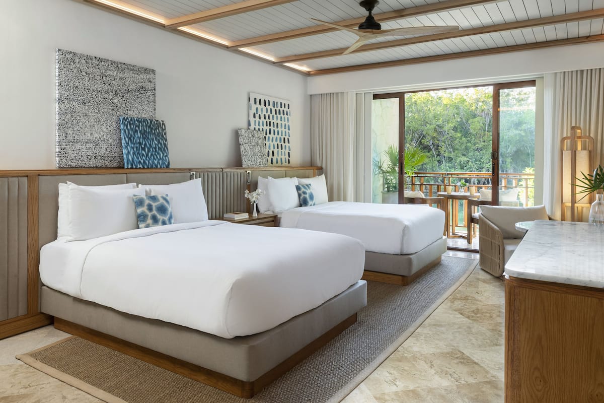 A hotel room with two beds, a balcony with a view of trees, and a wooden ceiling.