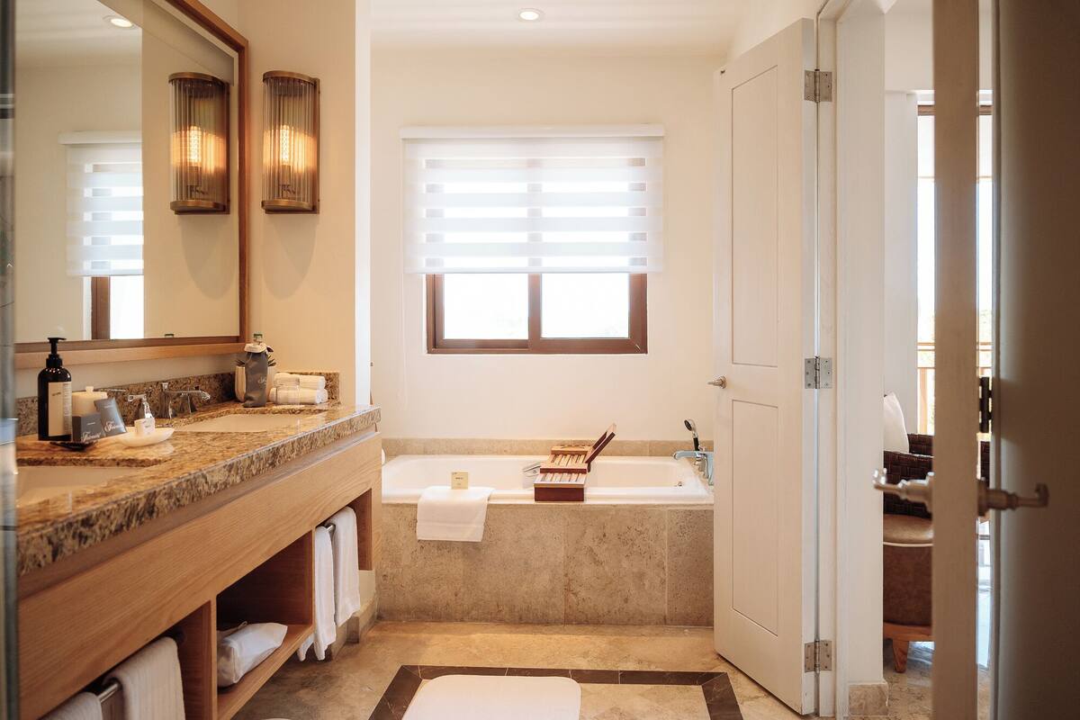 A bathroom with a bathtub, a vanity with a mirror, and a window with blinds.