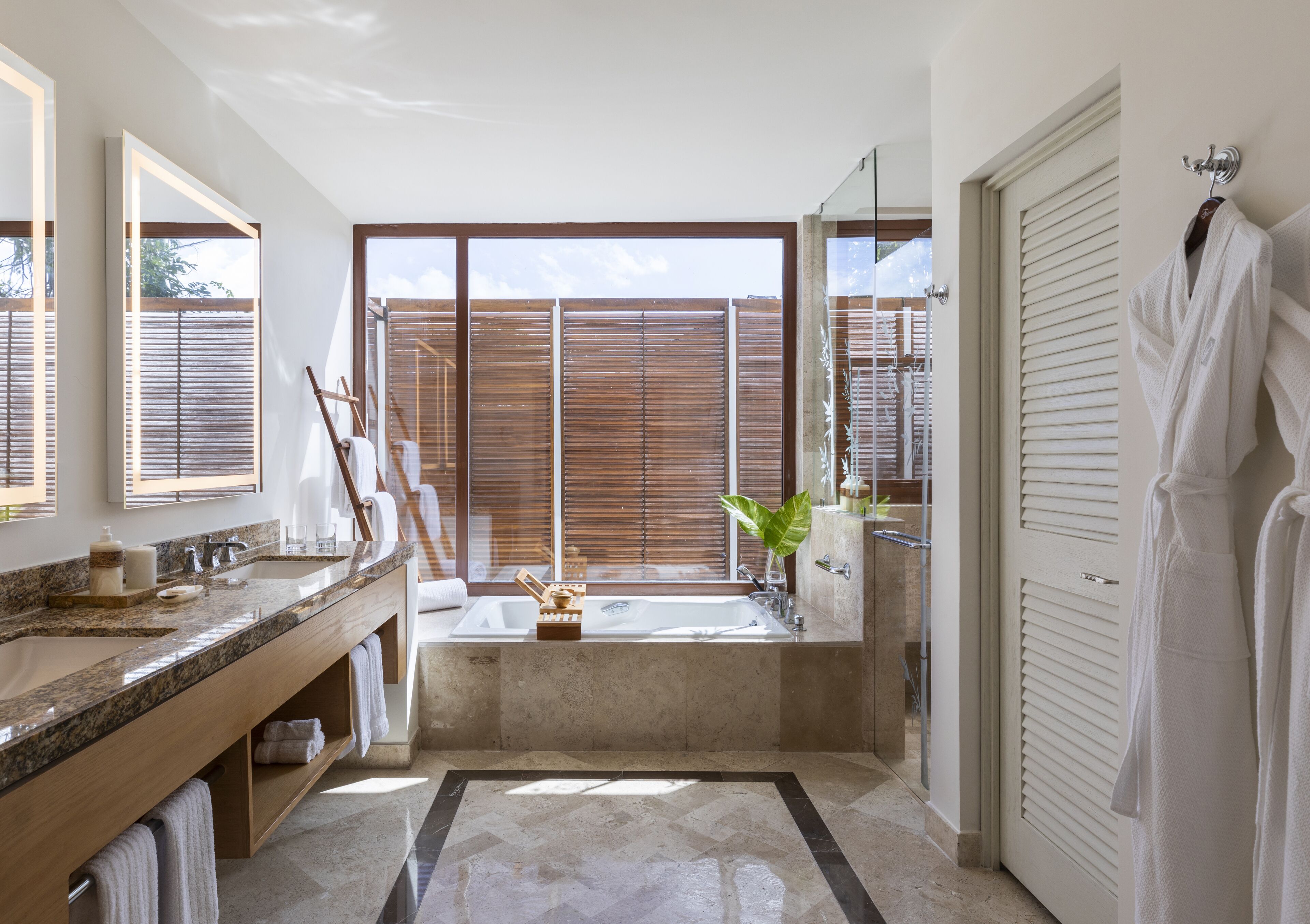 A modern bathroom with a large window, a bathtub, a vanity with a sink, and a robe hanging on the wall.