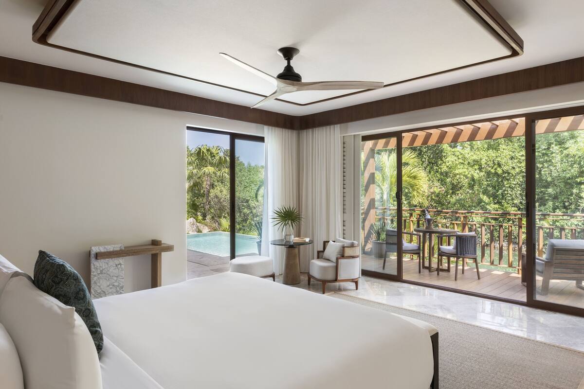 A spacious bedroom with a large bed, a ceiling fan, and a view of an outdoor deck with a pool and furniture.