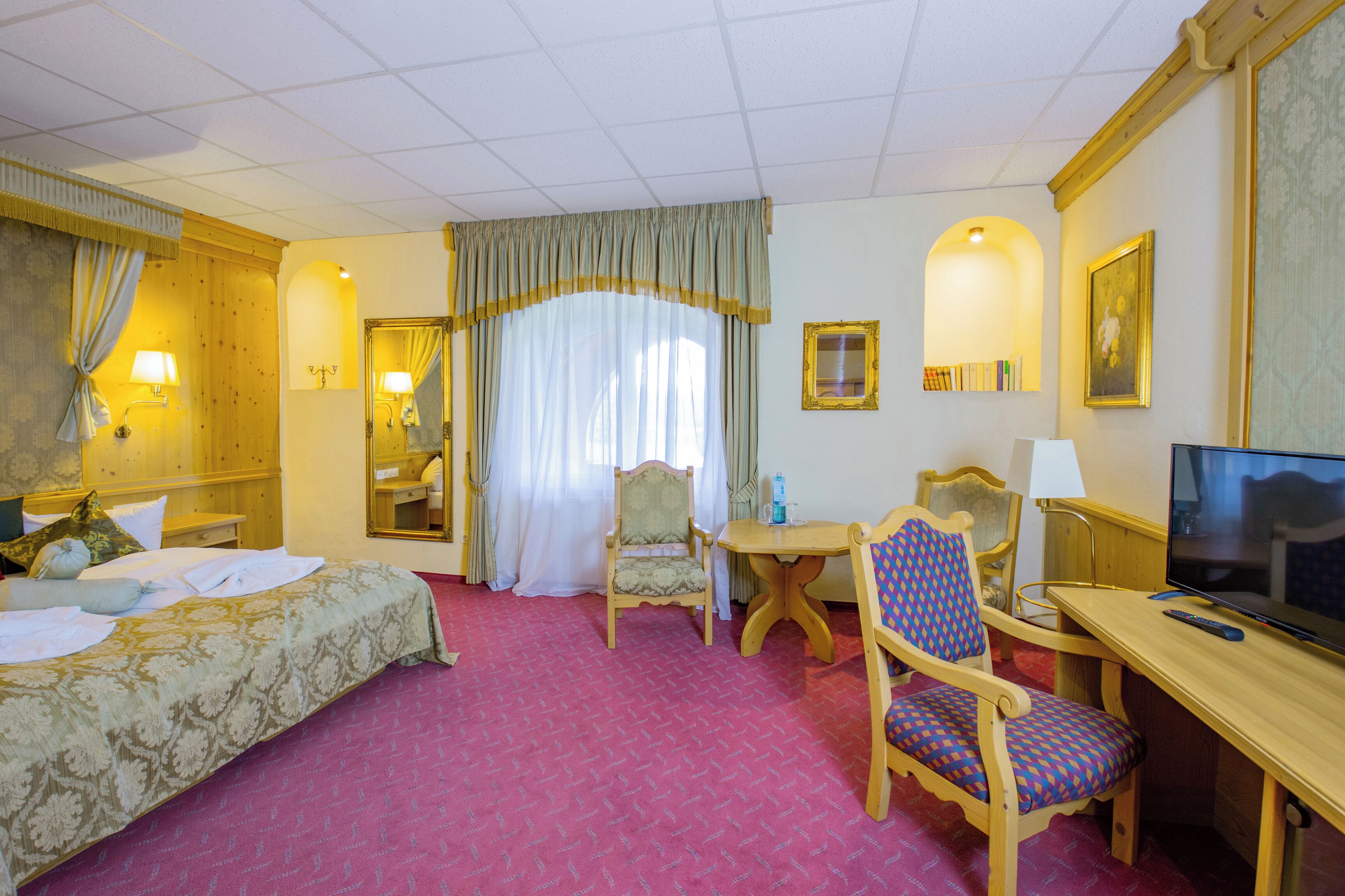 Habitación de hotel con cama, escritorio, televisor, silla y una pequeña mesa.