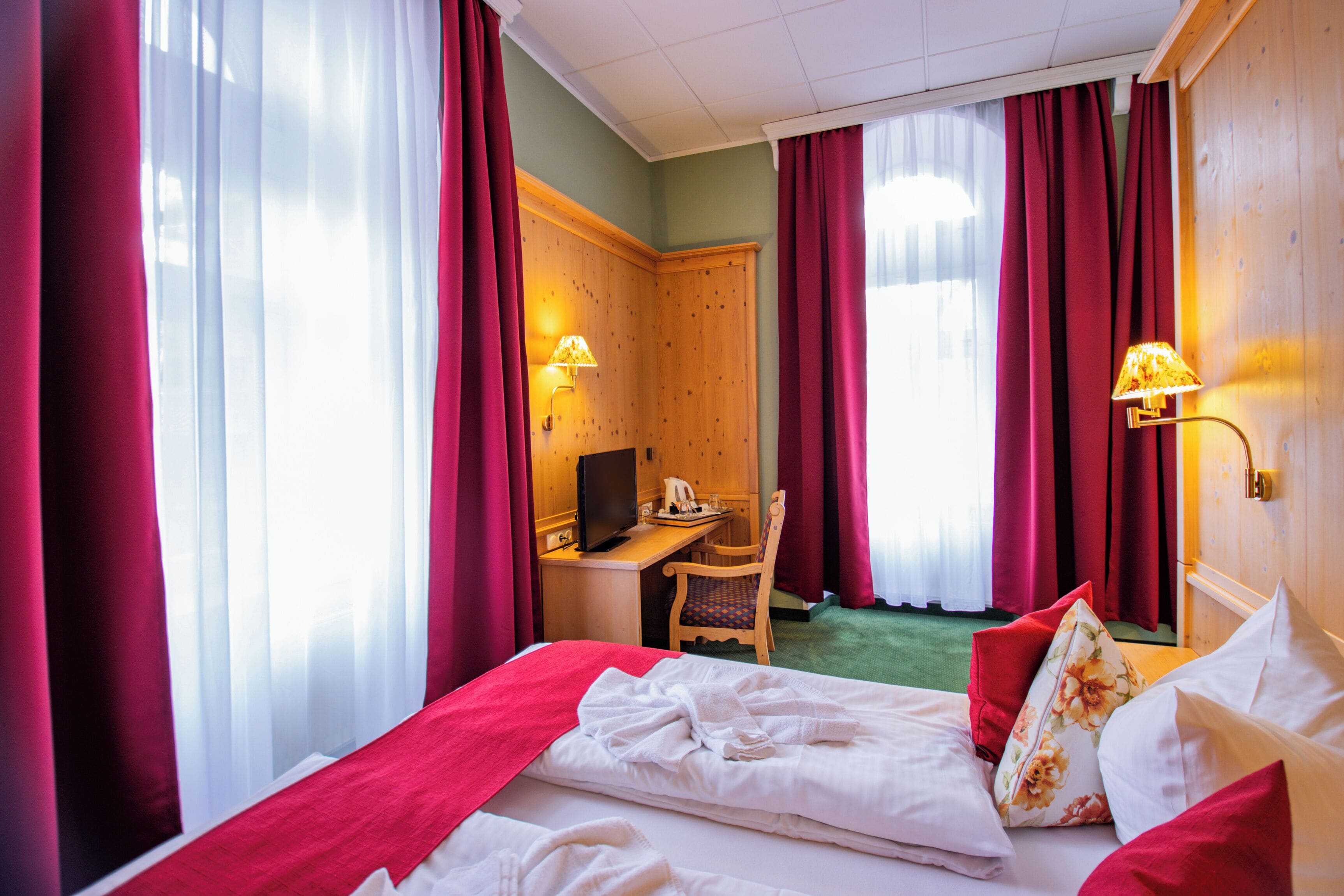 A hotel room with a bed, a desk, a chair, and a television.