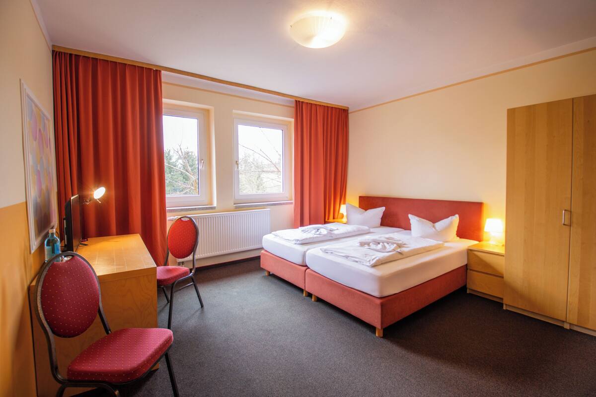 Ein Hotelzimmer mit zwei Betten, einem Schreibtisch, einem Stuhl und einem Kleiderschrank.