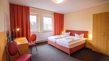 Ein Hotelzimmer mit zwei Betten, einem Schreibtisch, einem Stuhl und einem Kleiderschrank.