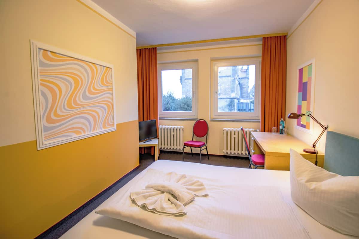 Ein Hotelzimmer mit einem Bett, einem Schreibtisch, einem Sessel, einem Fernseher und zwei Vorhängen.