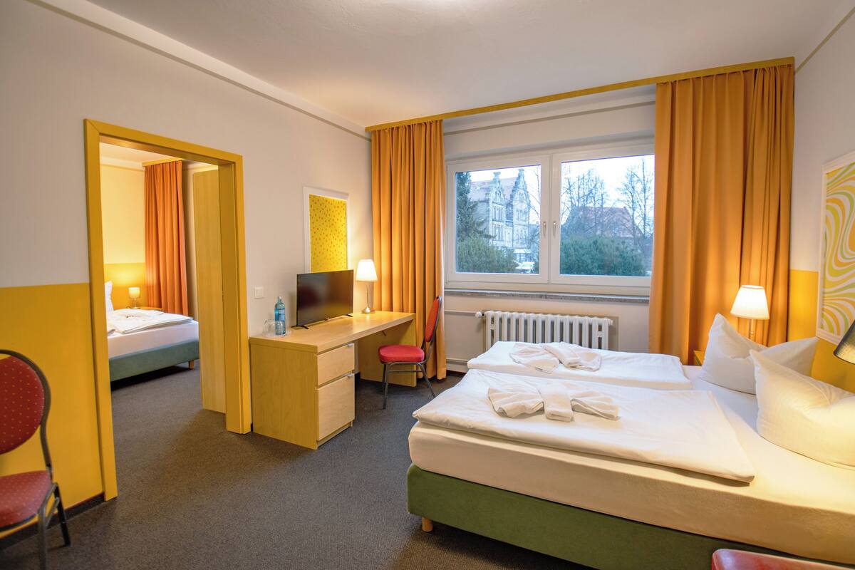 Ein Hotelzimmer mit zwei Betten, einem Schreibtisch, einem Stuhl und einem Fenster mit Vorhängen.