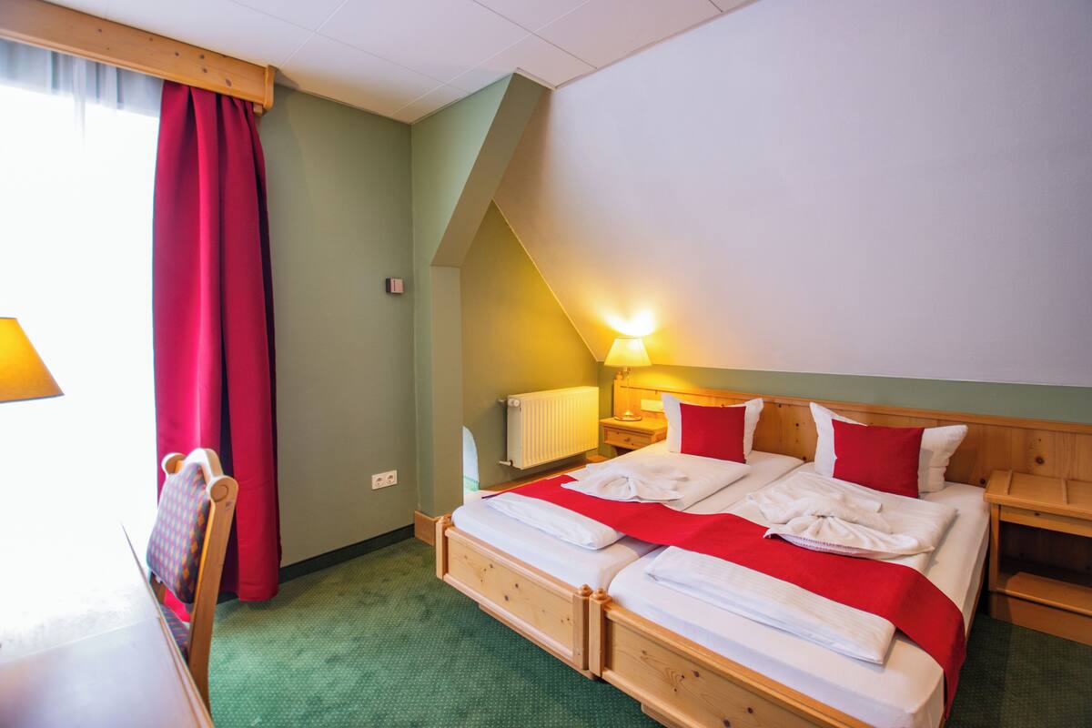 Ein Hotelzimmer mit Bett, Stuhl, Lampe und einem fenster mit Vorhängen.