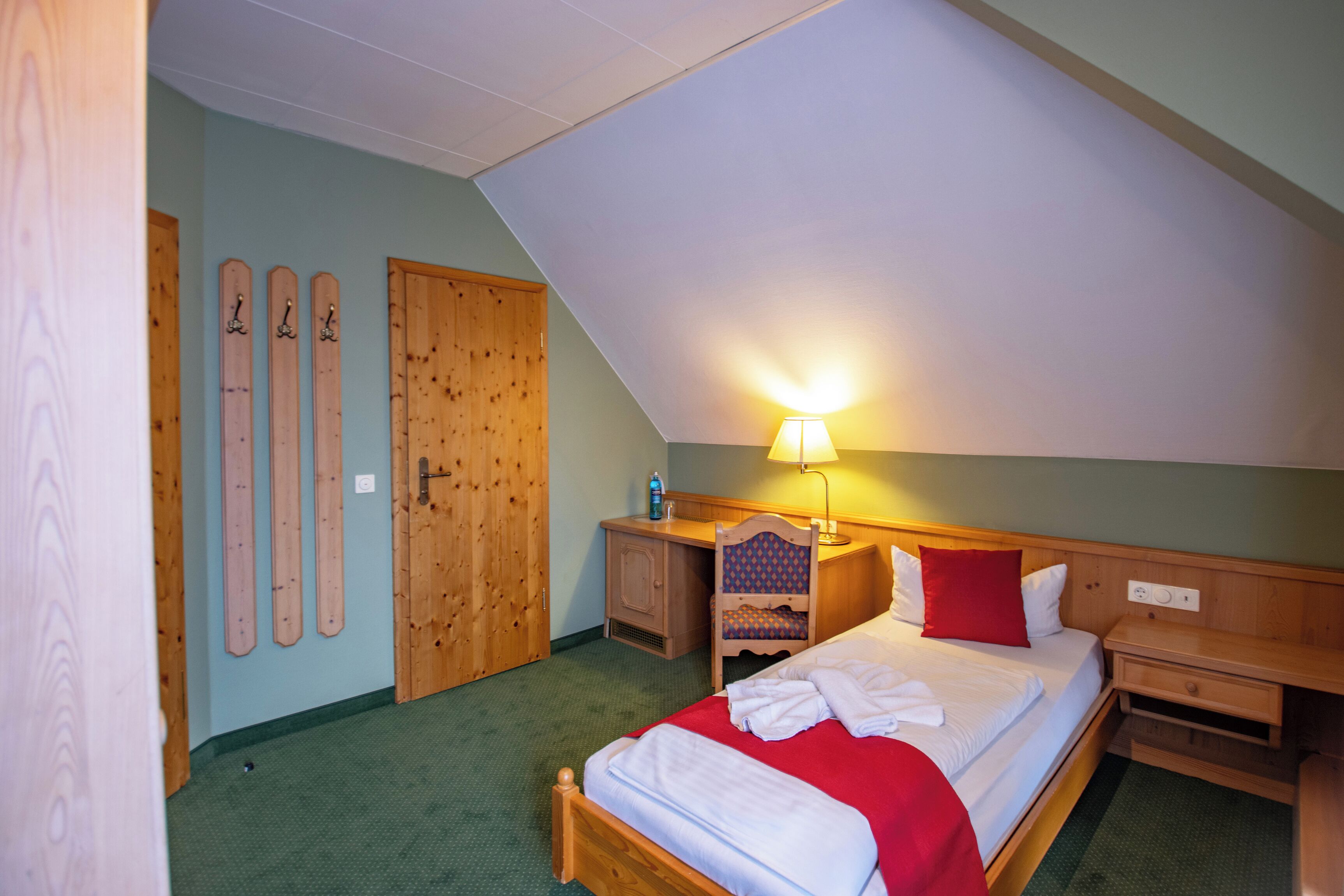 A bedroom with a sloped ceiling, a bed with white linens, a nightstand, a lamp, and a wooden wardrobe.