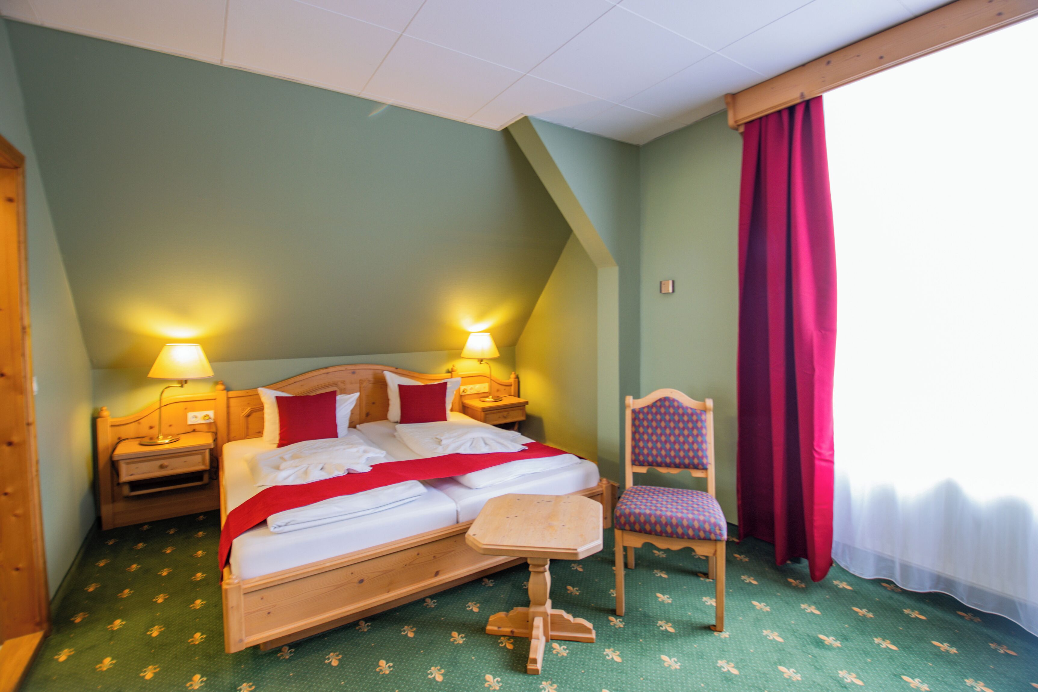 Et hotelværelse med en seng, to sengeborde med lamper, en stol og et vindue med gardiner.