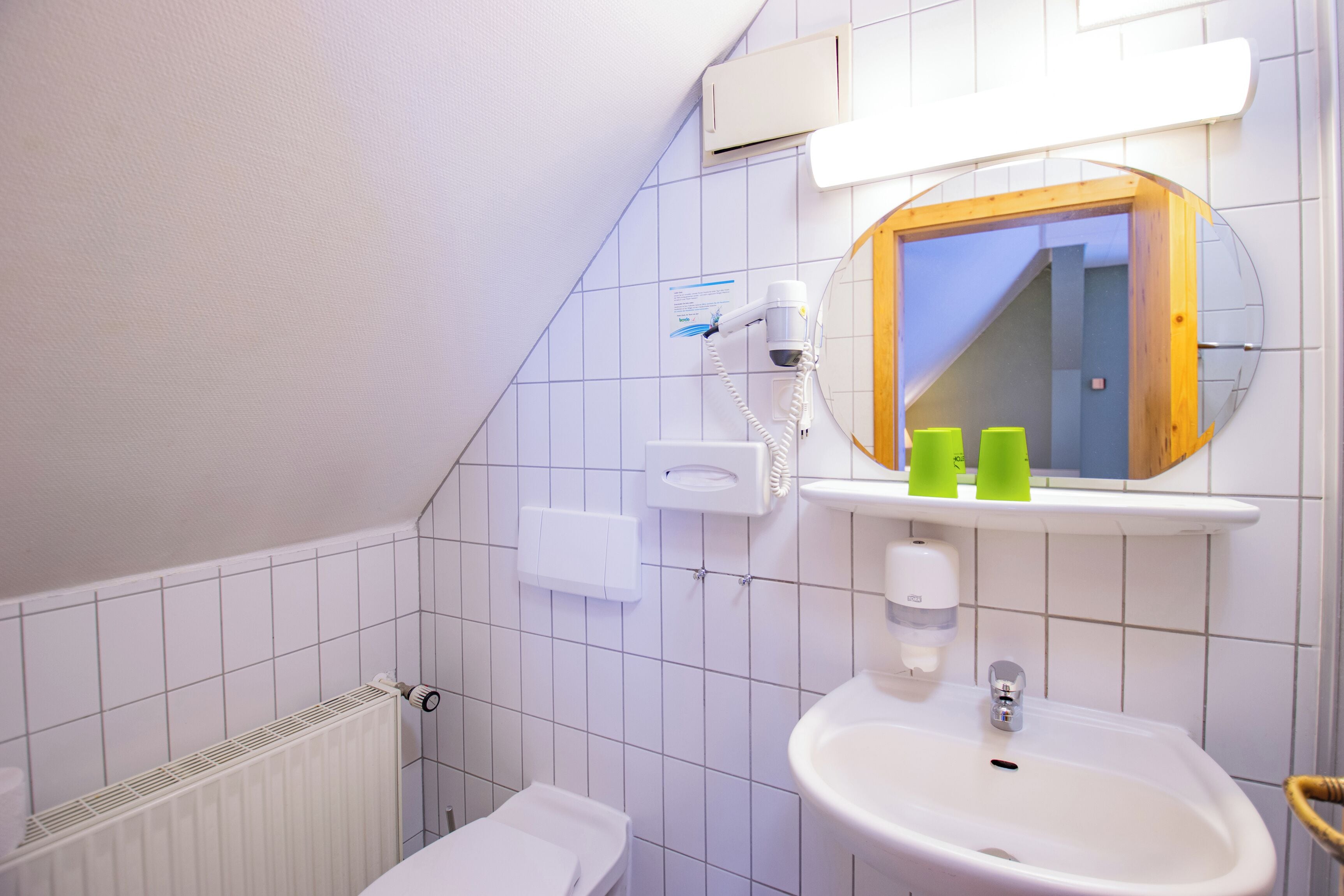 Ein Badezimmer mit einem weißen Waschbecken, einem Spiegel, einem Seifenspender und einem Haartrockner an der Wand.