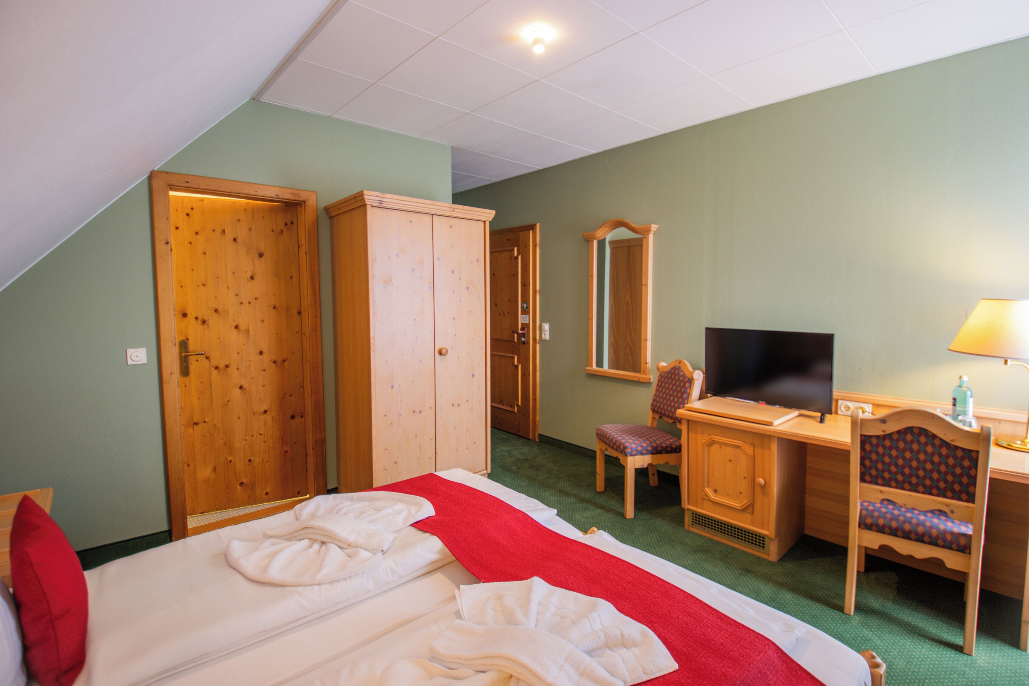 Habitación de hotel con cama, escritorio, silla, televisor y armario.