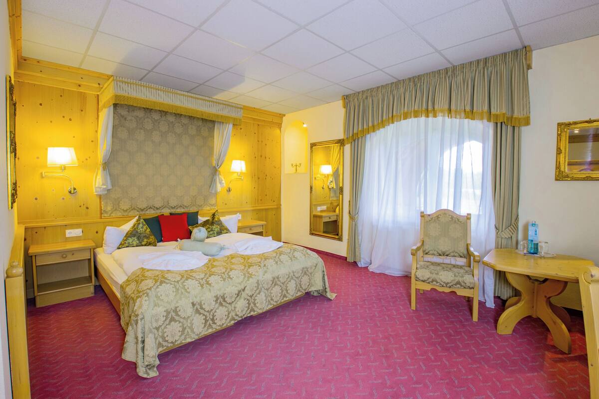 Ein Hotelzimmer mit einem großen Bett, einem Holznachttisch, einem Schreibtisch, einem Sessel und einem Spiegel.
