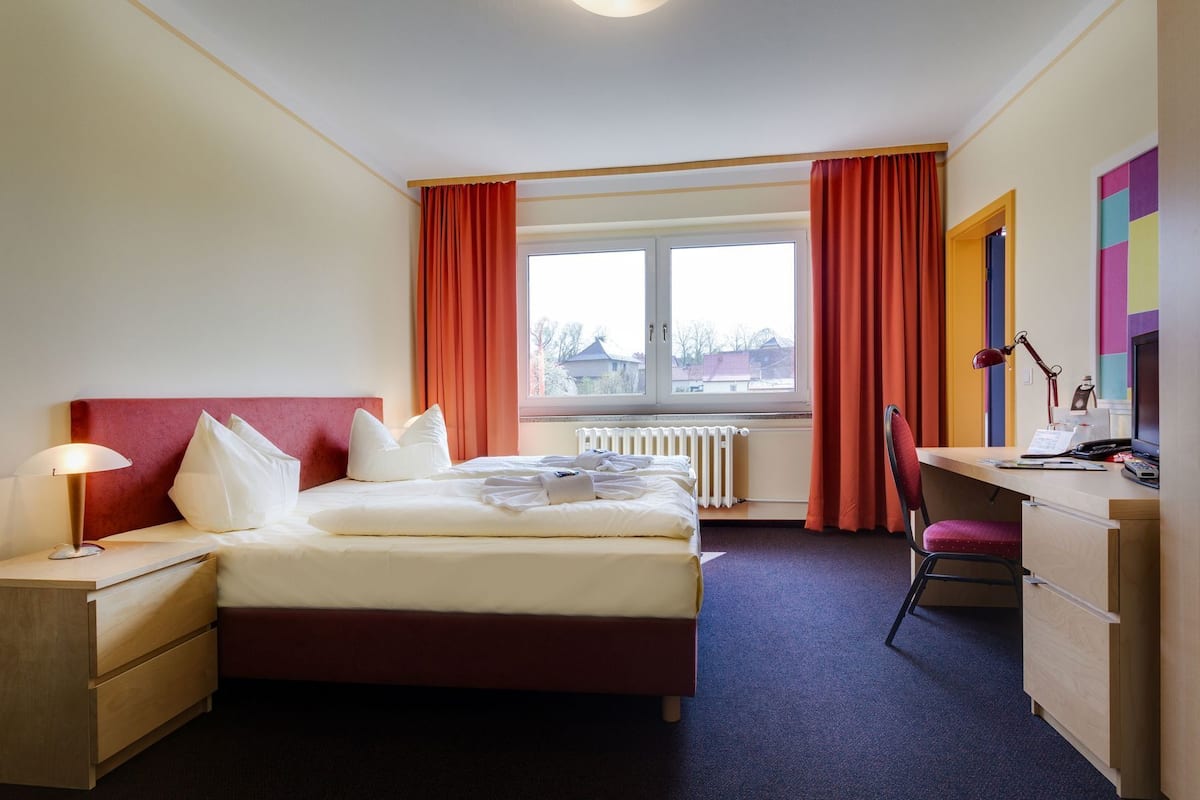 Ein Hotelzimmer mit Bett, Schreibtisch, Stuhl und einem Fenster mit Vorhängen.