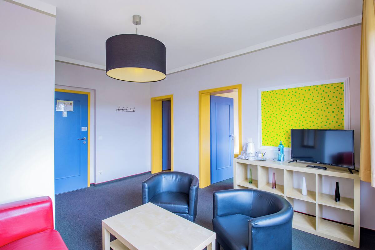 Ein Hotelzimmer mit Fernseher, zwei Sesseln, einem Tisch und einem Bücherregal.
