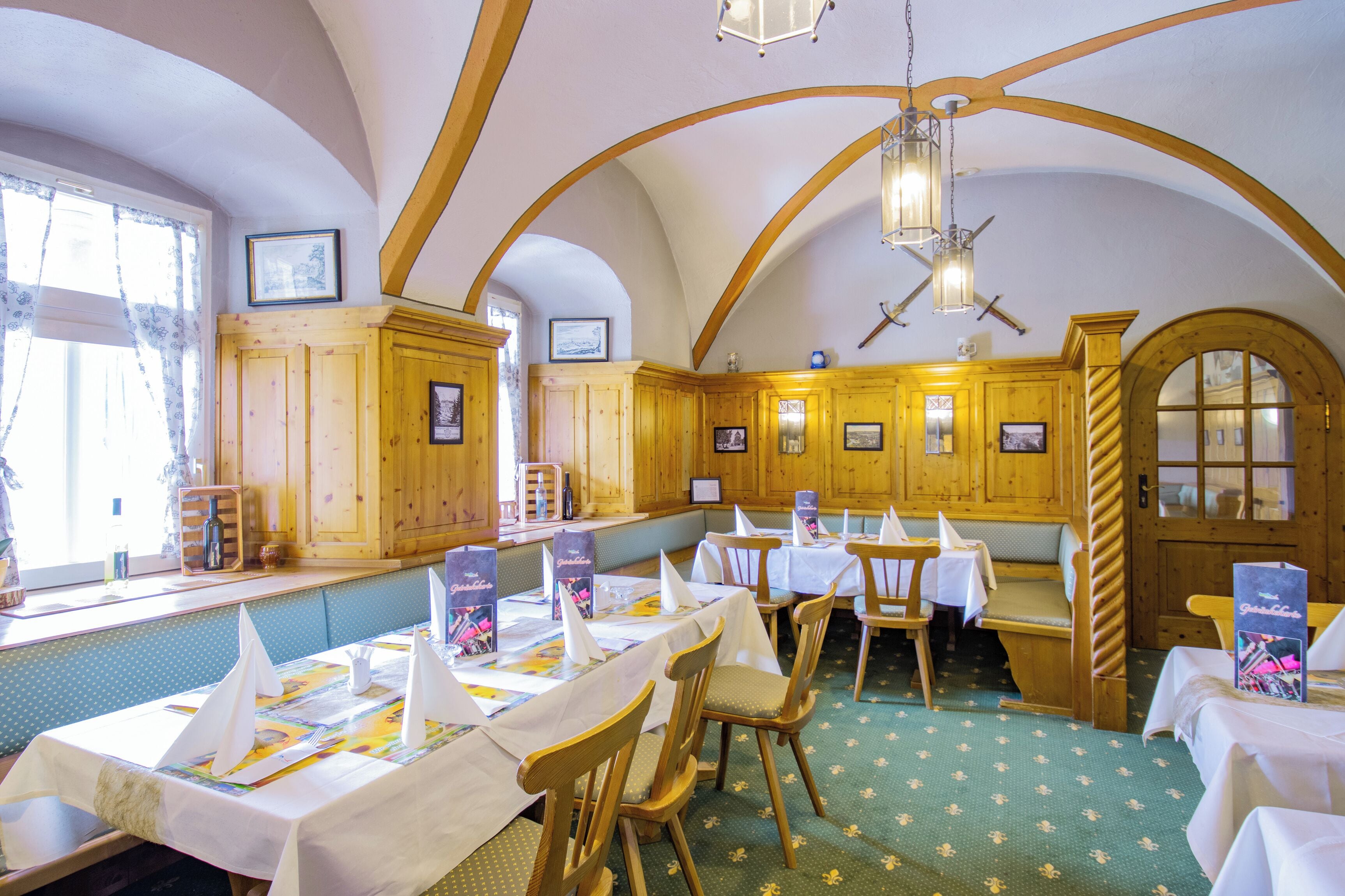 Un restaurante con interiores de madera, mesas dispuestas con manteles y servilletas blancas, y un suelo de diseño verde.